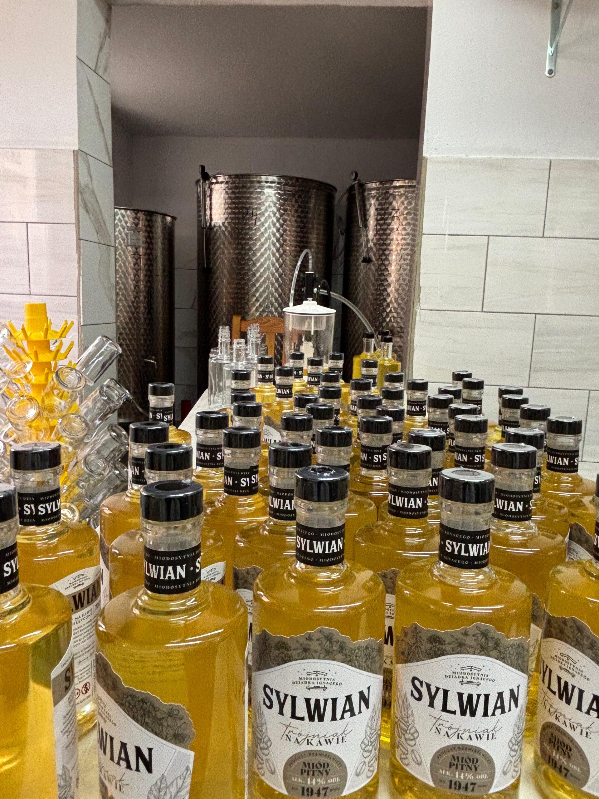 alt="SYLWIAN trójniak na kawie – nowa partia miodu pitnego w butelkach podczas rozlewu"